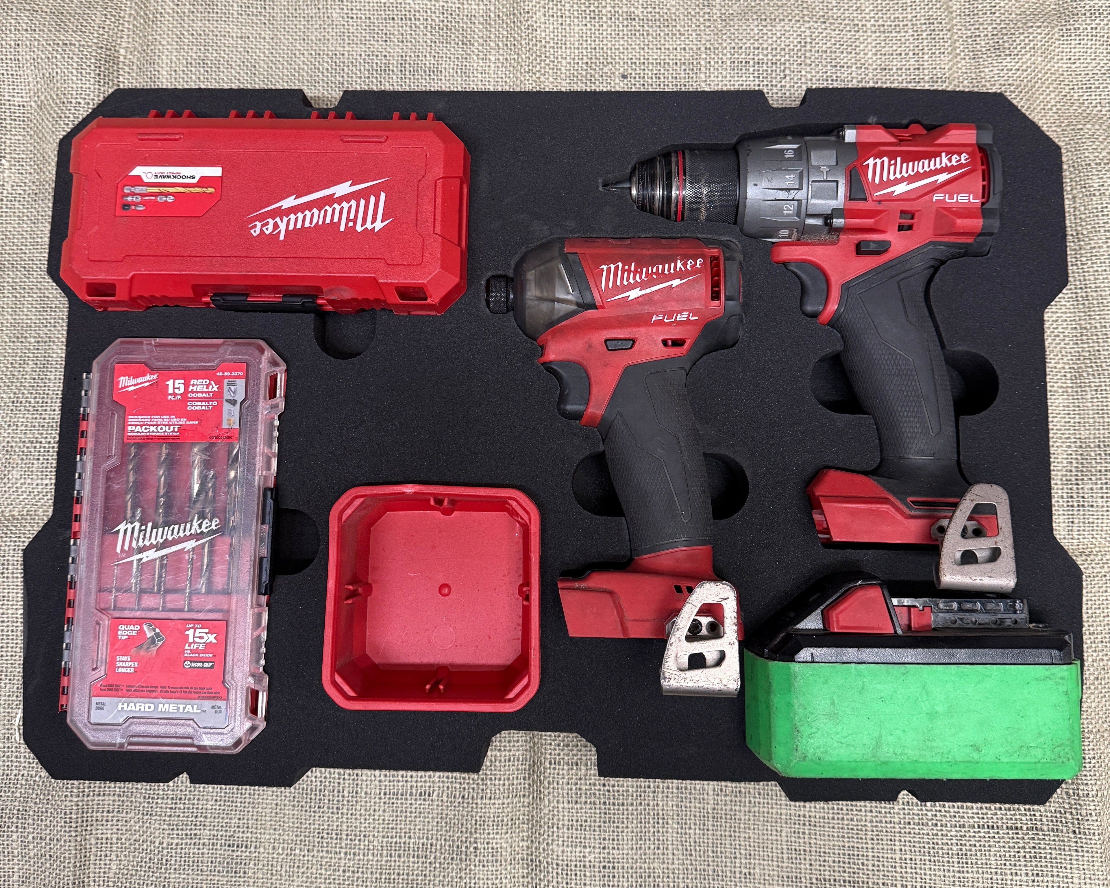 Milwaukee tool set with drill, impact wrench, and accessories on a textured surface